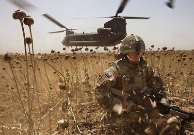 A U.K. Royal Marine crouches in a poppy field in Afghanistan as a Chinook helicopter lifts off. Photo: Defence Images.