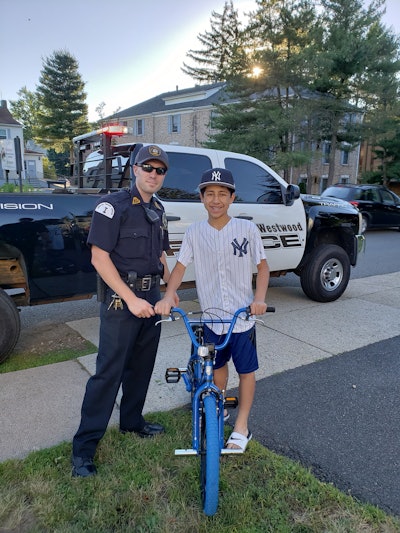Officer Ryan Sestanovich and 'Q,' the 13-year-old boy who Sestanovich helped to replace his stolen bike. (Photo courtesy of Westwood PD / Facebook)