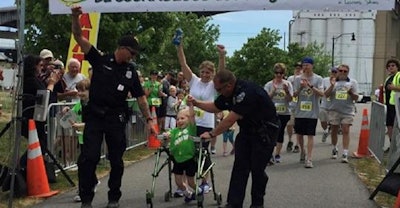 Officers Tim Wagner and Joe Donovan flanked little Easton Jordan for the duration of the walk as he worked relentlessly to cross the finish line of the 'walk, run, and roll' fundraiser to benefit the Make Lemon Aide Foundation for Cerebral Palsy. Image courtesy of Buffalo PD / Facebook.