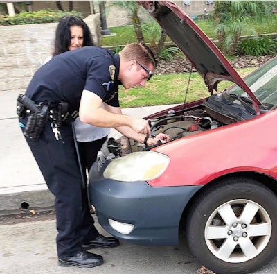An officer with the Long Beach (CA) Police Department was captured in an image making the rounds on social media installing a replacement car battery after a woman reported her original battery stolen. Image courtesy of LBPD / Facebook.