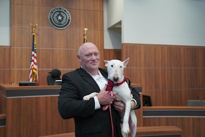 An officer with the Round Rock (TX) Police Department is now the proud owner of a three-year-old bull terrier that had suffered extensive injuries when it fell from the bed of a pickup truck and was dragged along the roadway for up to a mile before breaking free of its tether.