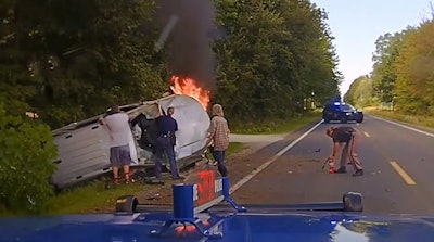 Dashcam video captures a Michigan state trooper using an ax to try to break through the windshiled of a burning car with the driver trapped inside.