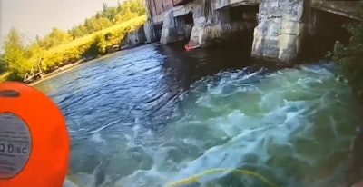 A Michigan state trooper prepares to throw a rescue device, with line attached, to a child trapped in the water at the base of a dam.