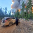 An officer with the Paradise Police Department stands beside a parked patrol vehicle and looks upon towering flames of wildfire.