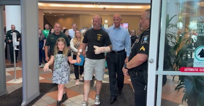 Wounded K-9 Handler Cpl. Matthew Aitken walks out of the hospital with his daughter and accompanied by Pinellas County Sheriff Bob Gualtieri.