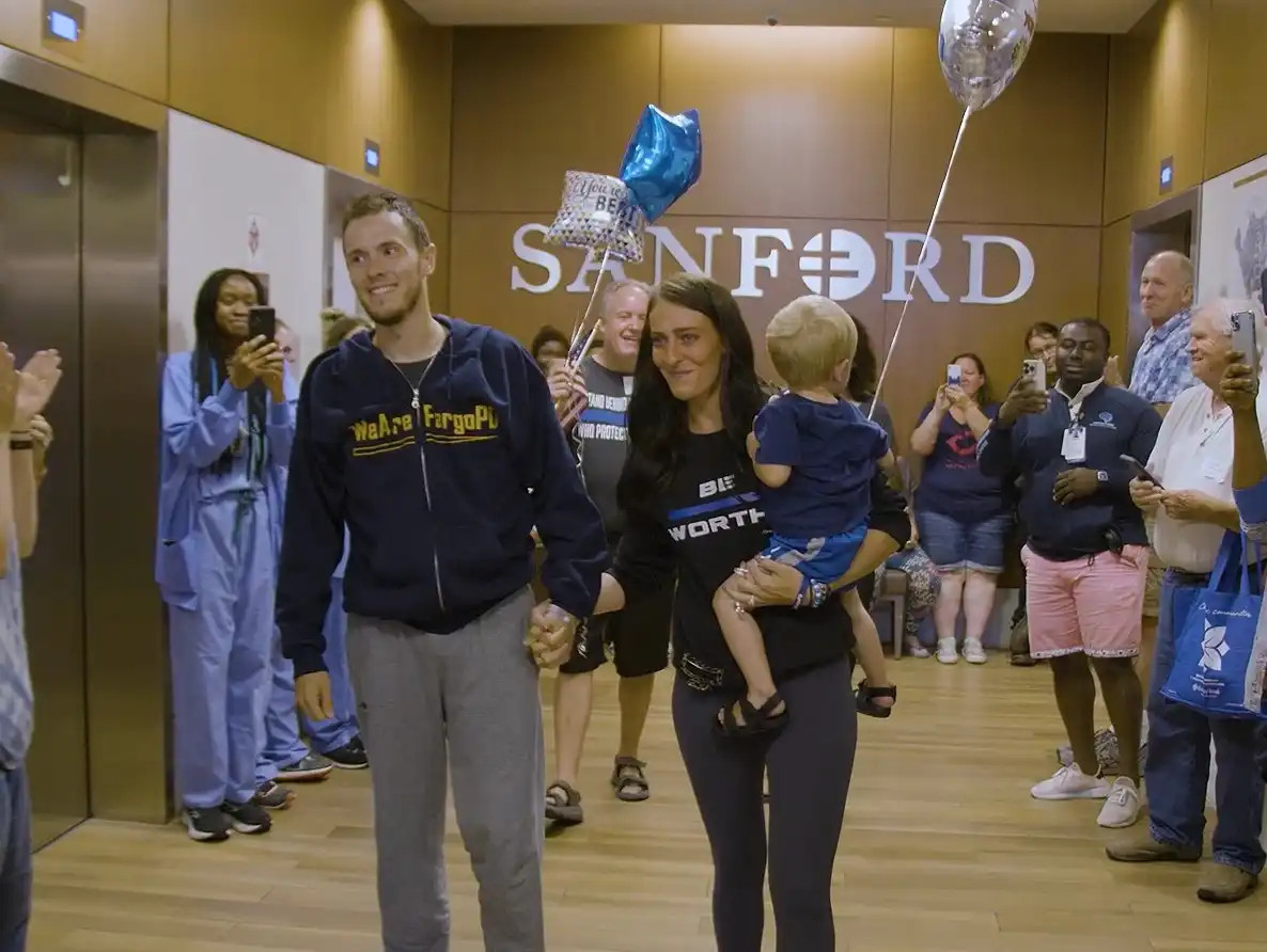 Fargo Police Officer Andrew Dotas walks out of the hospital with his wife and son. Dotas was wounded in a July 14 attack that also killed a fellow officer and wounded two more.