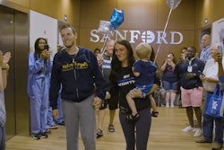 Fargo Police Officer Andrew Dotas walks out of the hospital with his wife and son. Dotas was wounded in a July 14 attack that also killed a fellow officer and wounded two more.