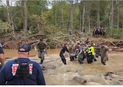 Responders transport an injured person across a flooded river.