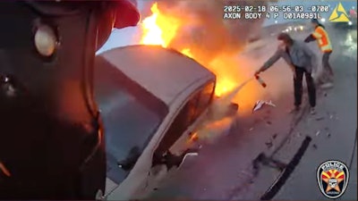 Motor Officer Brian Larison approaches a burning truck to smash a window so the female driver can escape from the wrecked vehicle.