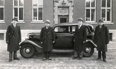 Officers are shown in front of a 1934 Ford Tudor.